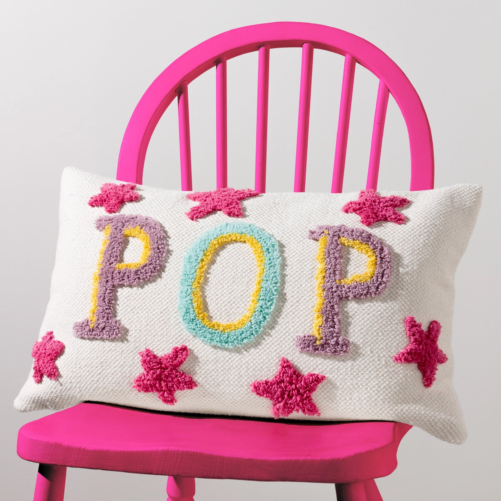 Decorative pillow with 'POP' and star patterns on a pink chair