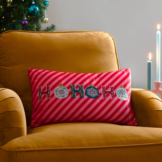 Pink striped pillow with 'HO HO HO' and Christmas ornaments on a mustard yellow armchair.